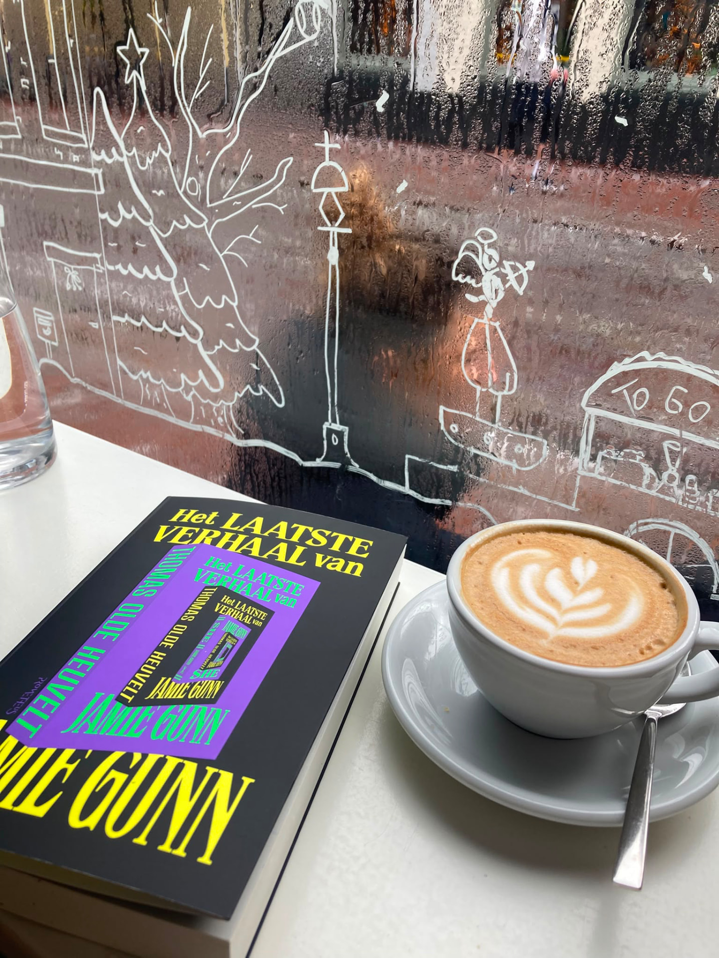 Een boek naast een cappuccino op een cafétafel in Den Bosch